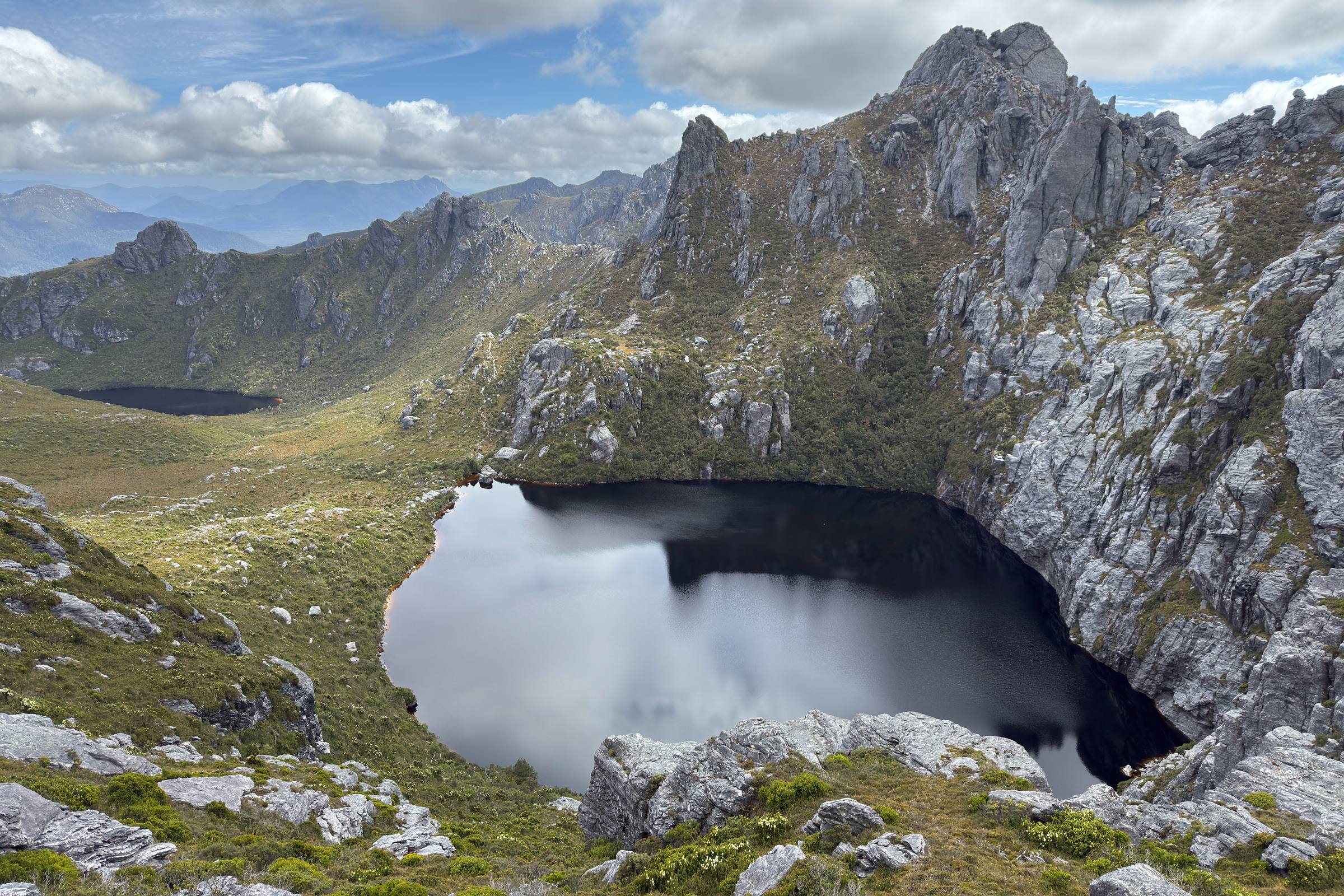 A dark tarn below a quartzite ridge in the Western Arthurs, Tasmania, with range after range fading out behind it.